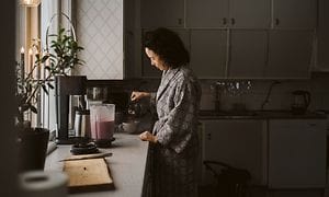 Keittiössä oleva nainen kaataa kuppiin kahvia ja tehosekoitin ja smoothie vieressä