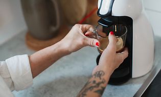 Keittiön pienlaitteet ja tarvikkeet - Nainen valmistaa kupillista kahvia kapselikeittimellä