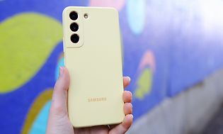 Henkilö on nostanut Samsung Galaxy S22 -puhelimen ilmaan, jossa on keltaiset silikonikuoret