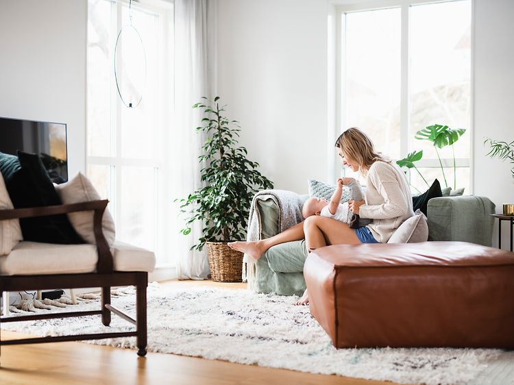 Nainen vauva sylissään istuu valoisassa olohuoneessa