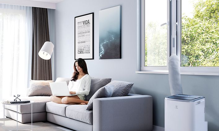 Electrolux - Sisäilman laatu - Siirrettävä ilmastointilaite sohvalla istuvan naisen vieressä