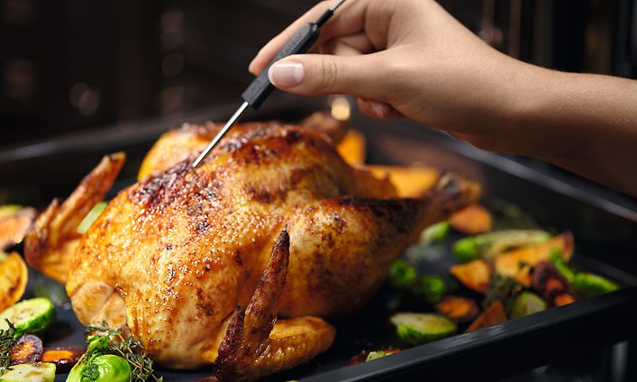 Electroluxin uunissa paistettu kana sekä käsi asettamassa siihen paistolämpömittaria