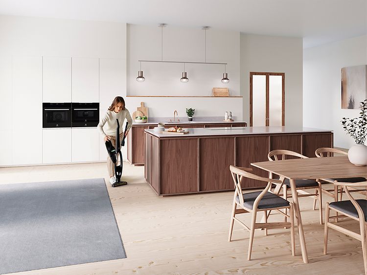 Nainen imuroi keittiön lattiaa Electrolux-varsi-imurilla