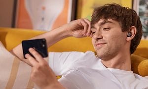 Jabra Elite 5 -kuulokkeet korvissaan oleva poika istuu sohvalla ja katsoo älypuhelintaan