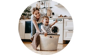 Keittiössä oleva äiti ja lapsi leikkivät pyykkikorilla