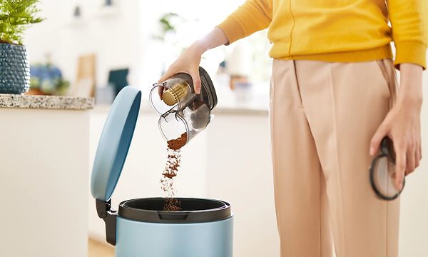 Henkilö tyhjentää pölynimurin pölysäiliötä roskikseen