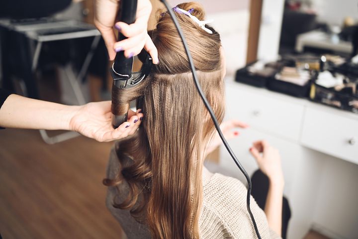 Stylisti tekee kiharoita naisen hiuksiin kihartimella kampaajalla