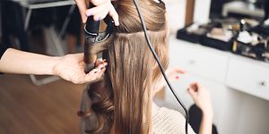 Stylisti tekee kiharoita naisen hiuksiin kihartimella kampaajalla