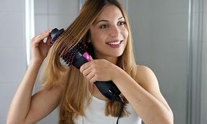 Nuori nainen käyttää pyöreää muotoiluharjaa hiusten muotoiluun kotona