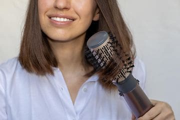 Nuori nainen stailaa ruskeita hiuksiaan muotoiluharjalla