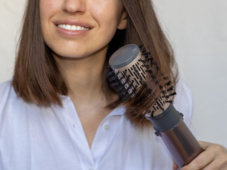 Nuori nainen stailaa ruskeita hiuksiaan muotoiluharjalla