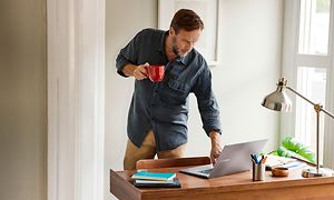 Google - Chromebook - kahvikuppia kädessään pitävä mies pitelee pöydällä olevaa Samsung Chromebook 4 -läppäriä