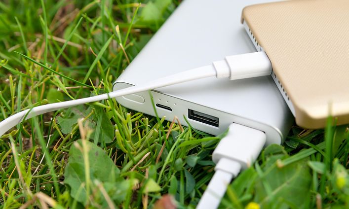 Ruohikossa oleva powerbank-varavirtalähde lataamassa älypuhelinta