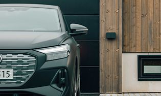 Seinälle kiinnitettävä Amina-autolaturi autotallin eteen pysäköidyn auton vieressä