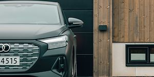 Seinälle kiinnitettävä Amina-autolaturi autotallin eteen pysäköidyn auton vieressä