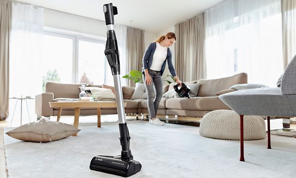 Bosch-pölynimurin quick stand ja nainen imuroimassa taustalla rikkaimuriosalla
