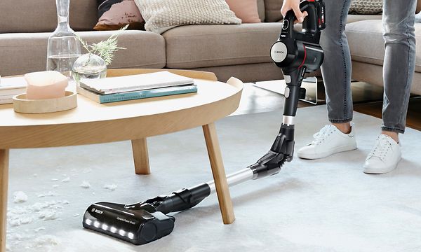 Nainen hyödyntää Bosch-pölynimurin taivutettavaa Flex tube -vartta siivotessaan huonekalun alta