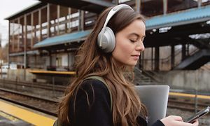 Nainen kävelee kuulokkeet korvillaan juna-asemalla