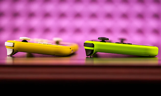 Keltainen ja vihreä Nintendo Switch Lite -konsoli pöydällä violettia taustaa vasten