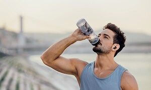 Mies juo vettä in-ear-kuulokkeet korvissaan