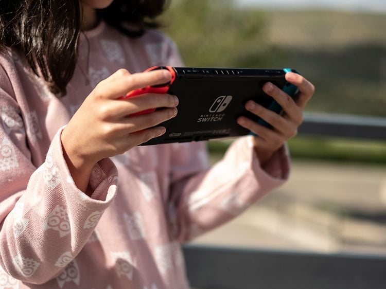 Kouluikäinen tyttö pitelee Nintendo Switch -konsolia kädessään ja pelaa sillä