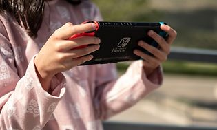 Kouluikäinen tyttö pitelee Nintendo Switch -konsolia kädessään ja pelaa sillä