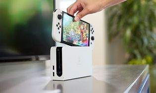 Henkilö asettaa Nintendo Switch OLED Model -konsolin sen telakointiasemaan