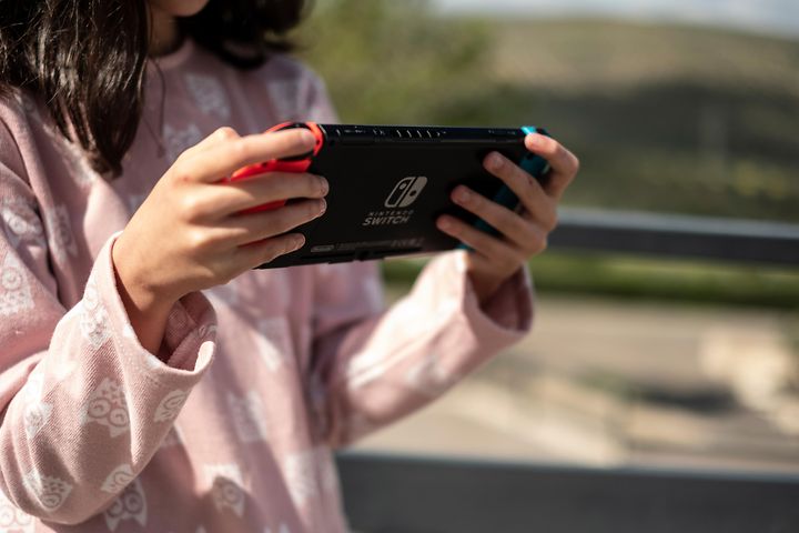 Kouluikäinen tyttö pitelee Nintendo Switch -konsolia kädessään ja pelaa sillä