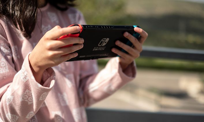 Kouluikäinen tyttö pitelee Nintendo Switch -konsolia kädessään ja pelaa sillä