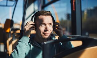 Mies bussissa laittaa kuulokkeita korvilleen