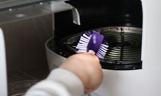 Joku puhdistaa airfryeria violetilla tiskiharjalla