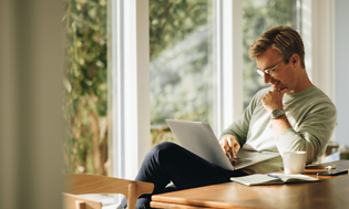 Hymyilevä mies istuu kannettavan edessä