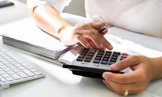 B2B - Nainen lepuuttaa kättänsä paperipinon päällä laskin kädessään
