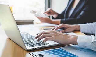 B2B - Kaksi toimistotyöntekijää, jotka työskentelevät hallinnon parissa kannettavalla tietokoneella ja laskimella
