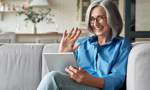 Nainen sohvalla hymyilee tablettia katsoen