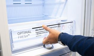 Miehen käsi avaa laatikkoa avoimen jääkaapin pohjalla