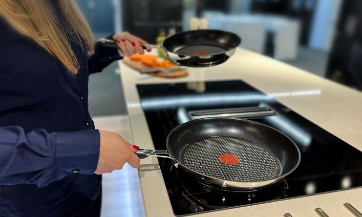 Nainen pitelee kahta paistinpannua keittotason yllä