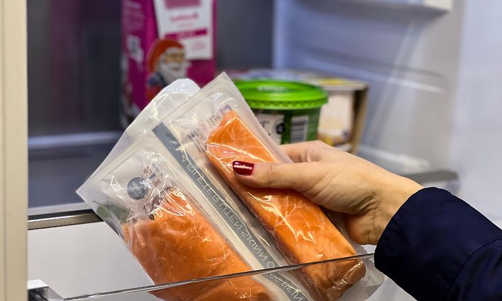 Käsi pitelee jääkaapista otettua kalapakettia