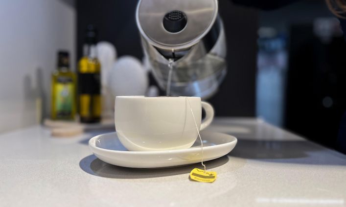 Henkilö kaataa kiehuvaa vettä vedenkeittimestä teekuppiin