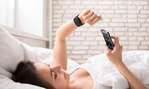 Nainen makaa sängyssä ja katsoo älykellon sykemittaria sekä puhelintaan