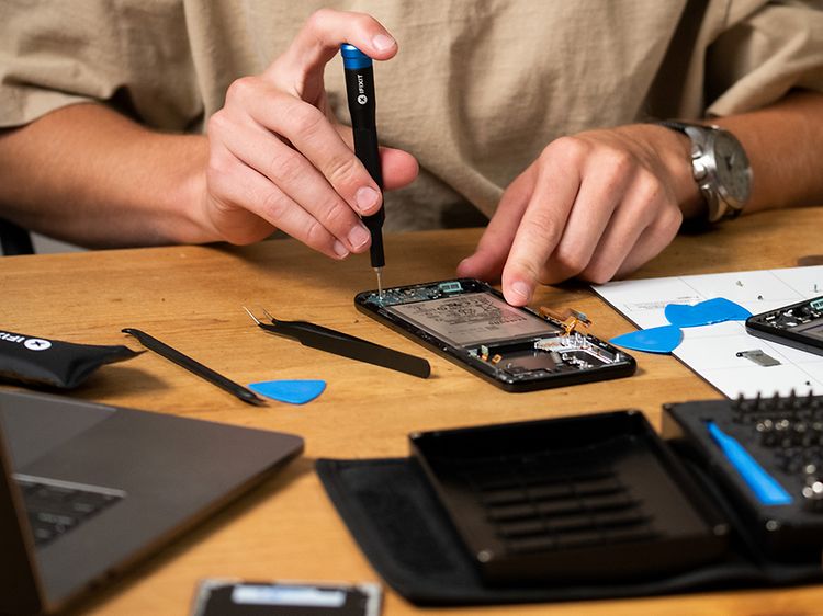 Mies korjaa älypuhelinta pienikokoisella iFixit-ruuvimeisselillä