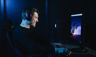 Pelaaja istuu näytön edessä hymyillen