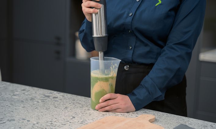 Gigantin naispuolinen myyjä valmistaa smoothieta sauvasekoittimella