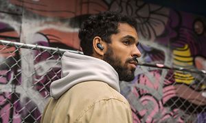 Graffititausta sekä huppariin pukeutunut mies kuuntelee Bose Earbuds -nappikuulokkeilla