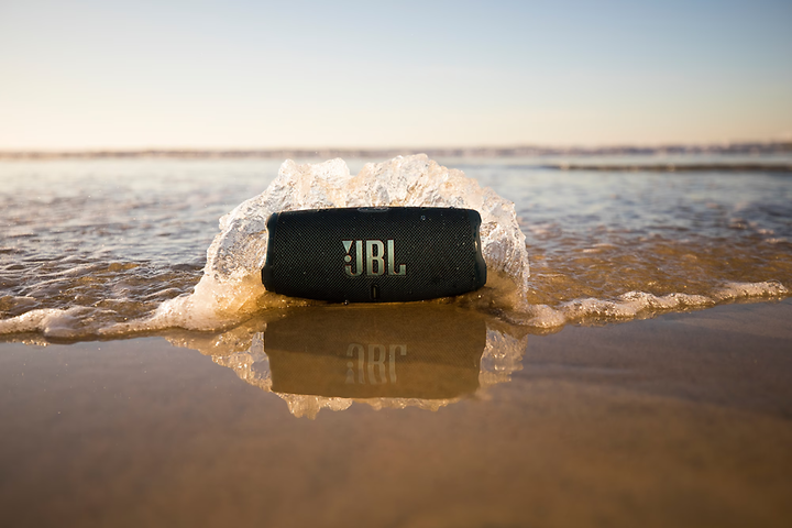 JBL Charge 5 -kaiutin rannalla, jossa aallot lyövät kaiutinta vasten