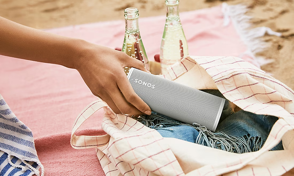 Nainen asettaa Sonos Roam -kaiutinta kangaskassiin, joka on piknipeiton päällä rannalla