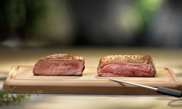 Kaksi mehevää palaa pihviä leikkuulaudalla ja veitsen sen vieressä