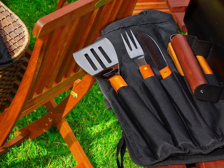 Erilaisia grillausvälineitä nurmikolla piknik-korin vieressä