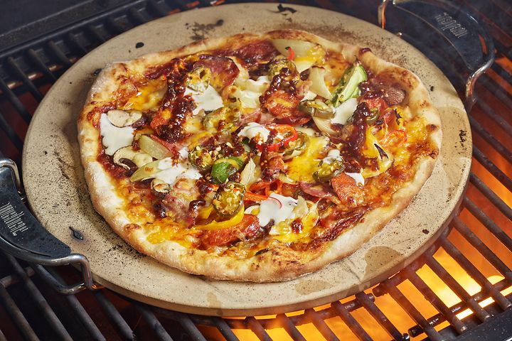 Pizzakiven päällä oleva pizza paistumassa grilliritilällä