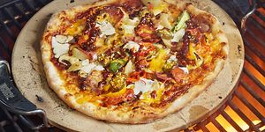 Pizzakiven päällä oleva pizza paistumassa grilliritilällä